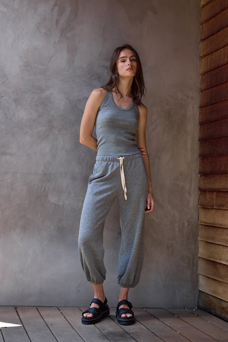 Woman wearing a gray  baby rib tank  top and  gray sweatpants standing against a textured wall.