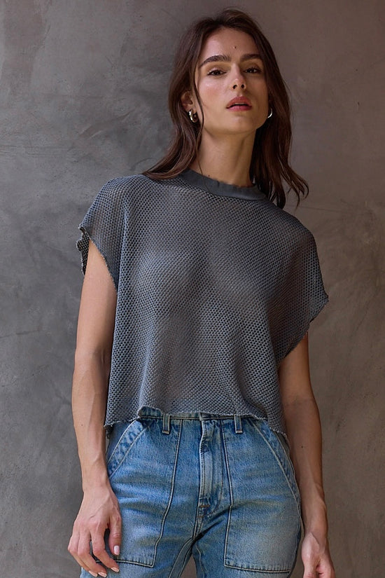 Woman wearing a mesh gray top and blue jeans against a brown background