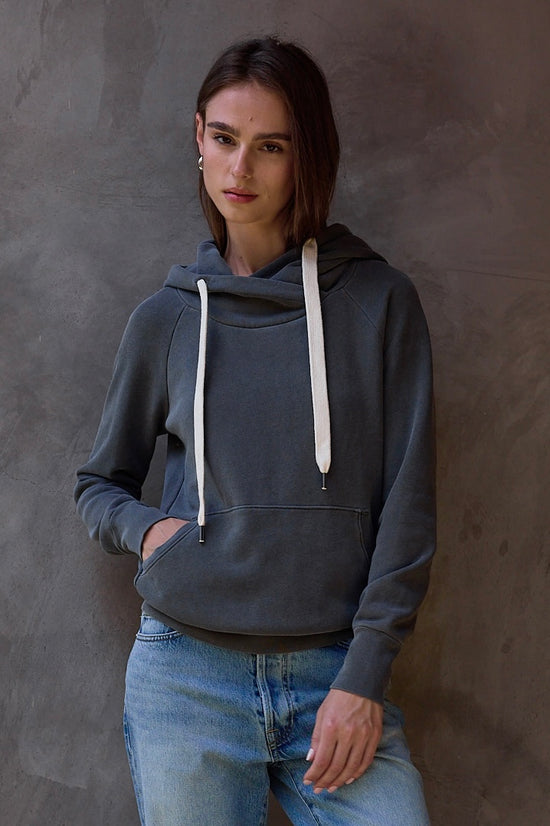 Woman wearing a dark gray hoodie with white drawstrings against a textured brown wall.