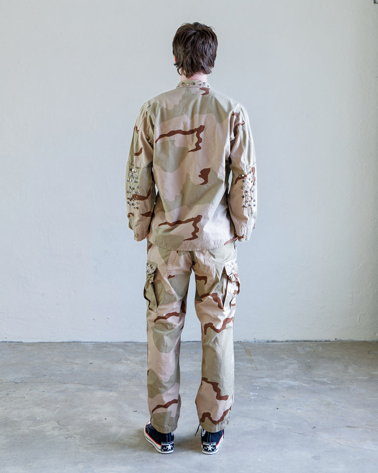 Model wearing the Scout Studded Twill Unisex Cargo Pant - Desert from the back with a military camouflage shirt.