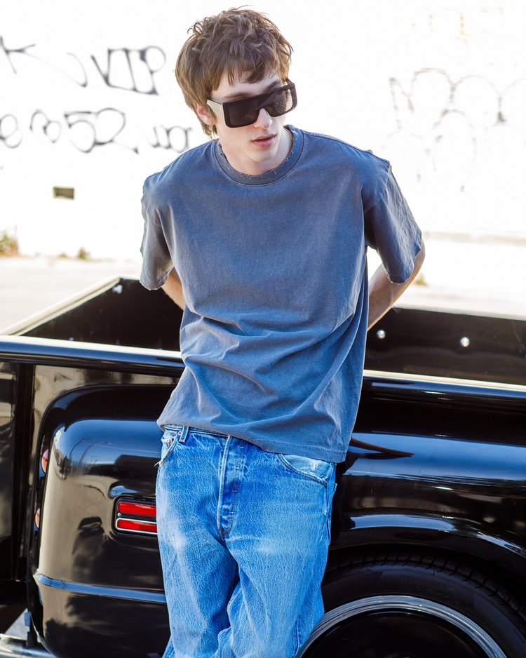 Person wearing a blue tee shirt and jeans leaning against a black 1960 chevy truck.