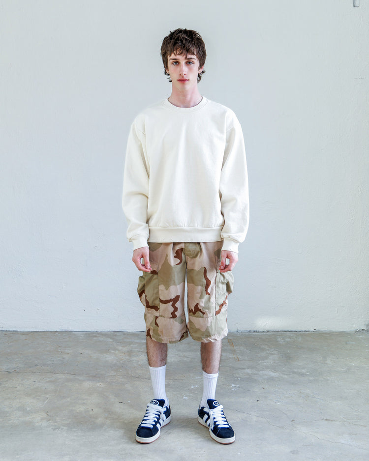 Model wearing Jesse Twill Unisex Cargo Short - Desert with a white sweatshirt and sneakers, showcasing desert camo style.