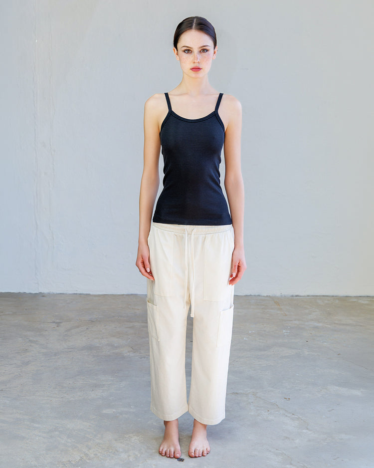 Model wearing Kai Rib Cami Tank - Black with loose white pants, showcasing its slim-fit design and stylish look.