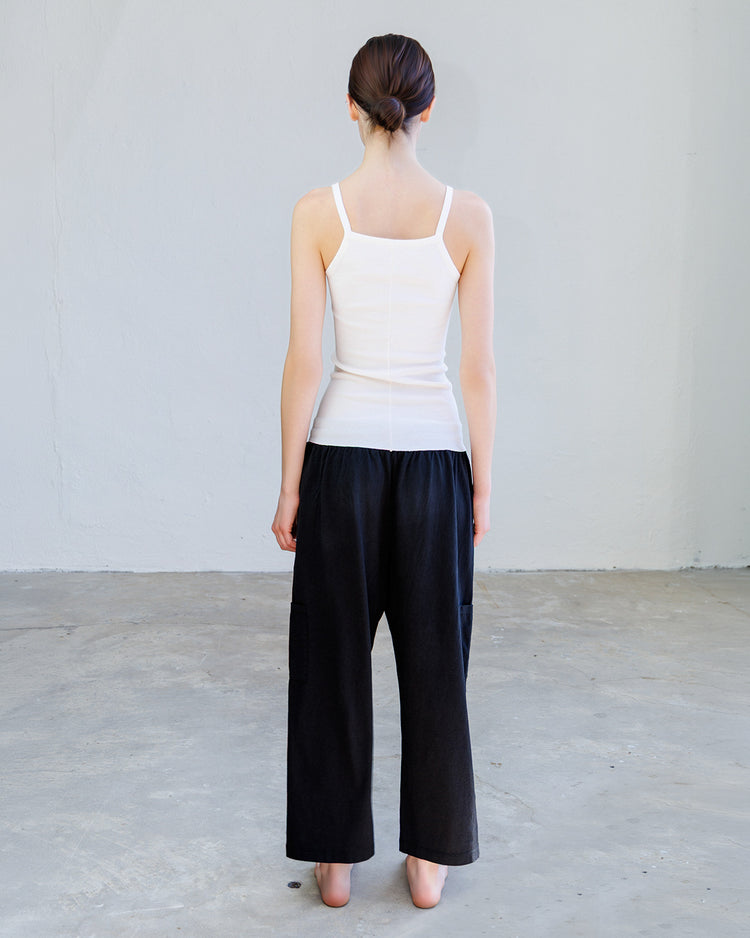 Back view of a model wearing the Kai Rib Cami Tank - Pearl paired with loose black pants.