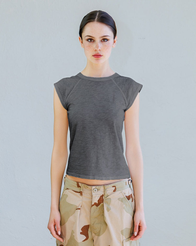 Woman wearing a gray cap sleeve top and camouflage chorts against a plain background